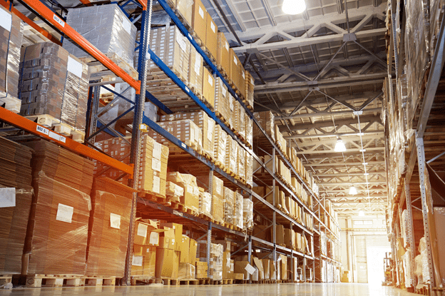 Warehouse aisle with packed boxes and pallets with light shining at the end of the hall