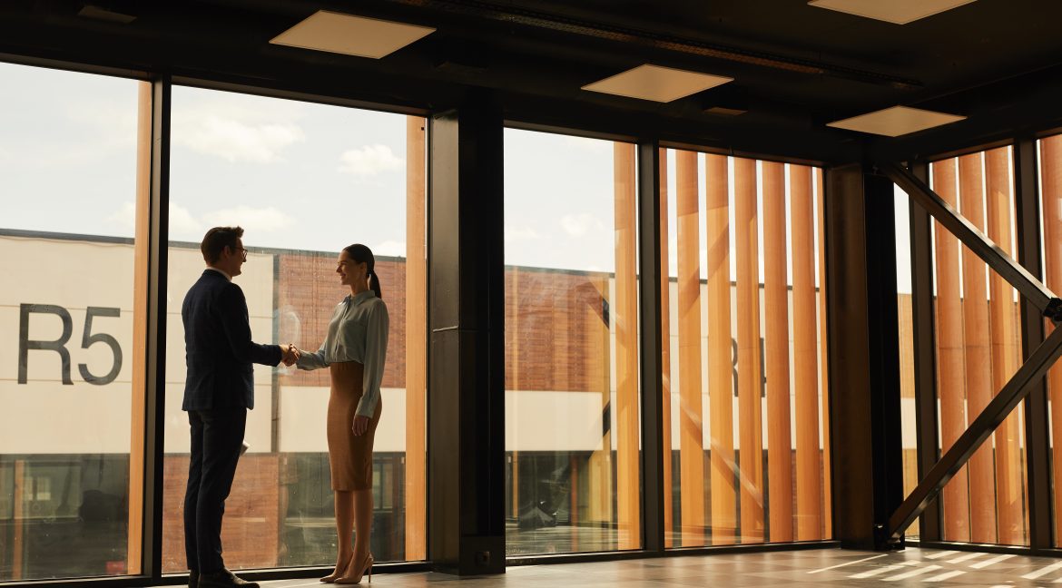 real estate agent shaking hands with client while standing in empty office building commercial space for rent